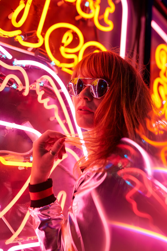 Portrait of woman with silver jacket and sunglasses in neon lights
